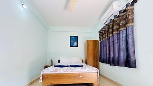 A bedroom with a bed, a wardrobe, a nightstand, a wall-mounted air conditioner, and a patterned rug. - Blue Stay Inn Holiday Home - Near Baga Calangute Beach (Calangute)