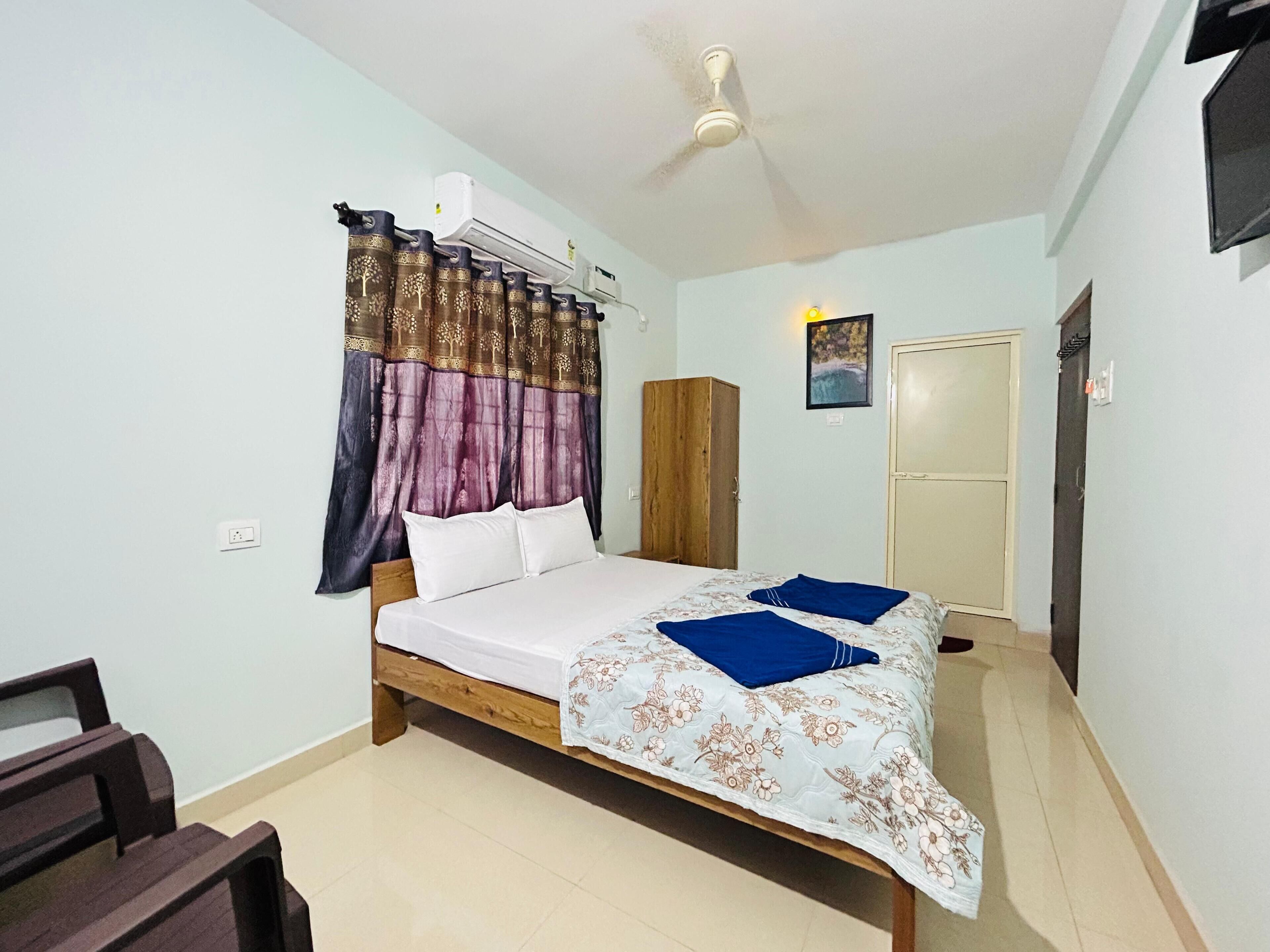 A bedroom with a bed, a wardrobe, an air conditioning unit, a ceiling fan, and a door.