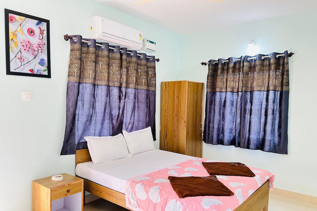 A bedroom with a bed, a wooden wardrobe, and an air conditioning unit.
