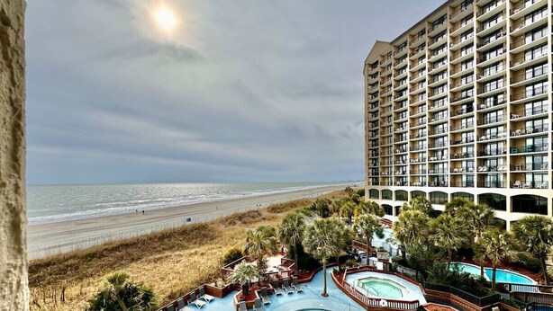 A hotel with a pool area, beach view, and multiple balconies. - Tropical Resort 1BR 307 (North Myrtle Beach)