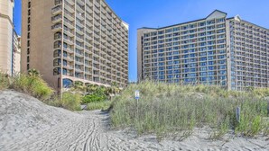 A beachfront hotel with multiple high-rise buildings, sandy paths, and sparse vegetation. - Tropical Resort 1BR 307 (North Myrtle Beach)