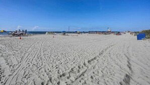 A wide sandy beach with footprints, a lifeguard tower, and beach umbrellas. - Tropical Resort 1BR 307 (North Myrtle Beach)