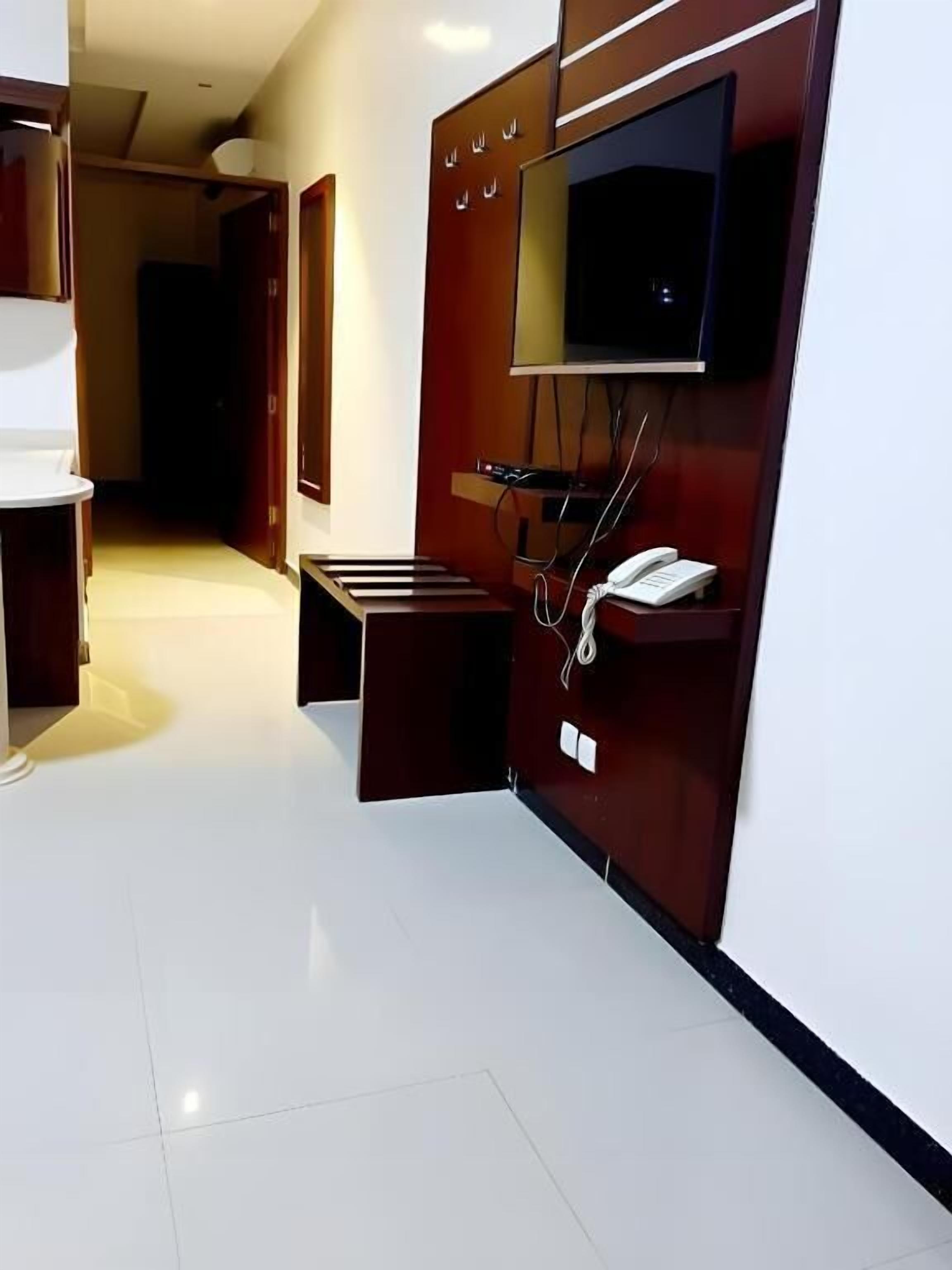 A hotel room with a flat-screen TV mounted on the wall, a bedside table with a phone, and a small seating area.