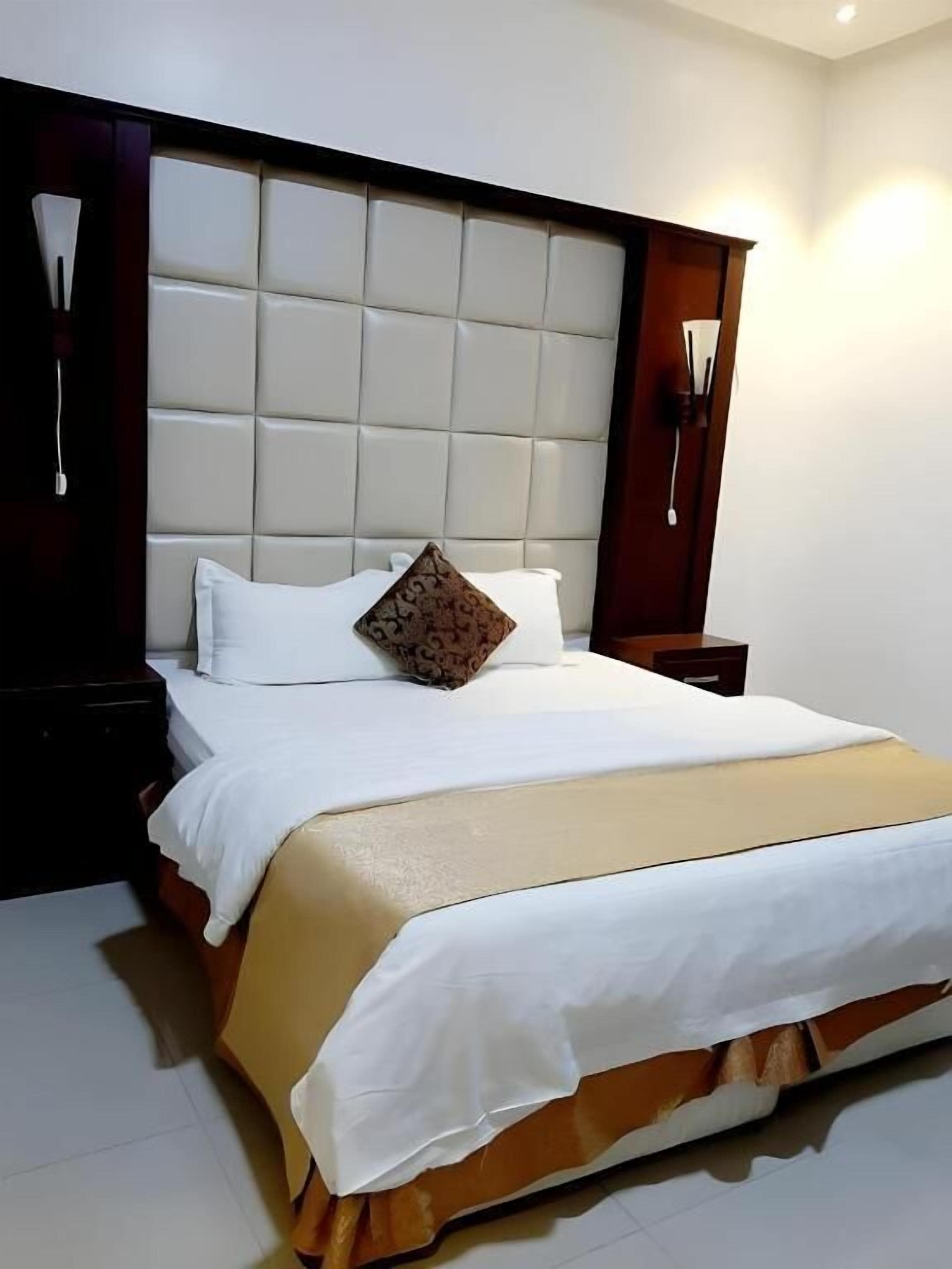 A hotel room with a large bed, a padded headboard, and a bedside table.