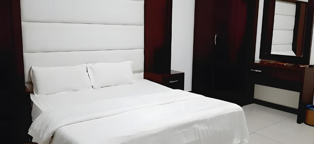 A neatly made bed with white linens in a room with a dark wood headboard and a large mirror.