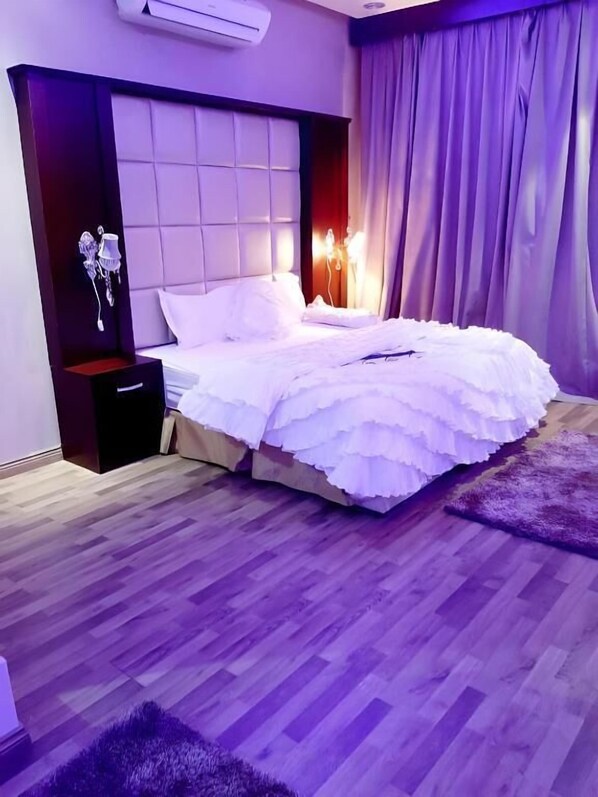 A bedroom with a large bed, a nightstand, a dresser, and a wall-mounted air conditioner. - Ahlin Suites 3 (Riyadh)