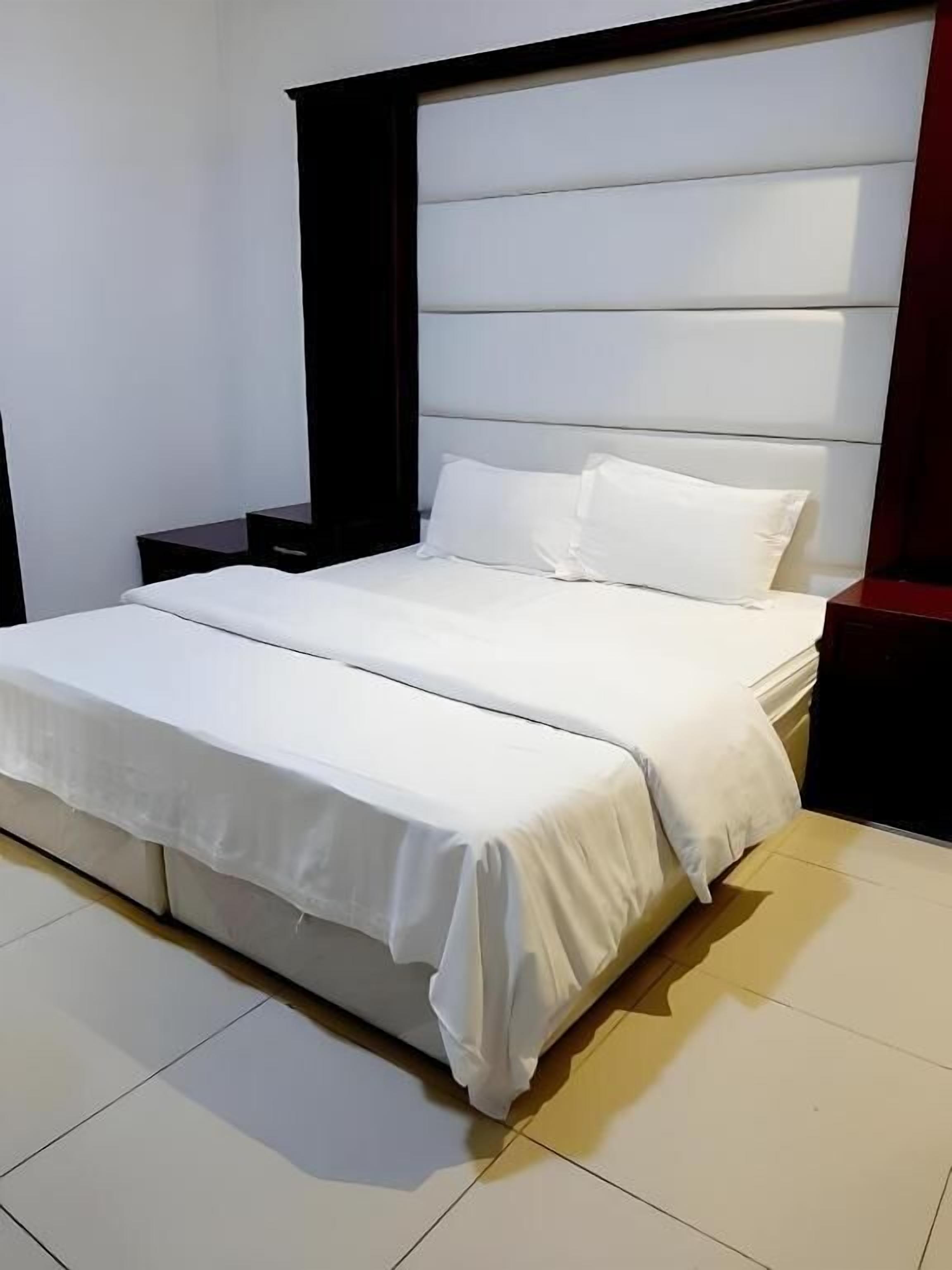 Une chambre à coucher moderne avec un grand lit, une literie blanche et une tête de lit sombre.
