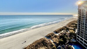 A beachfront hotel with a pool, ocean view, and a clear sky. - Tropical Resort 1BR 1407 (North Myrtle Beach)