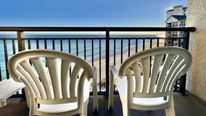 Two white plastic chairs and a small table on a balcony with a view of the ocean and a building in the background. - Tropical Resort 1BR 1407 (North Myrtle Beach)