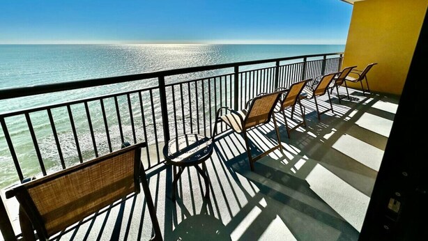 A balcony with a view of the ocean, featuring a railing and two chairs.