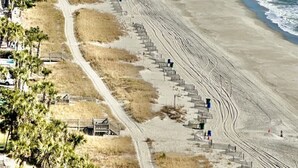 A coastal beach with a long, sandy shoreline, a clear blue ocean, and a few people walking along the beach.