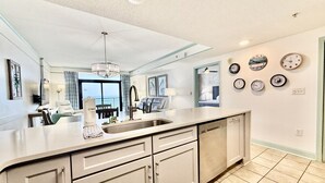 A modern kitchen with a large island, a built-in dishwasher, and a variety of clocks on the wall.