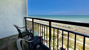 En balkon med udsigt over stranden, en pool og en stol.