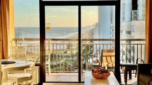Un balcone con vista sull'oceano e sulla città, arredato con un tavolo, sedie e un cesto.