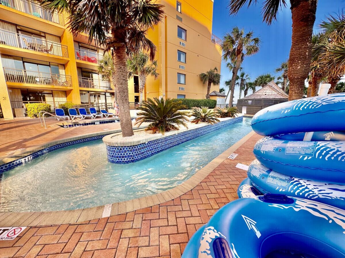 A hotel pool area with blue inflatable rings, palm trees, and a tiled pool edge.