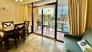 Ein Zimmer mit Esstisch und Stühlen, einer Couch und einem Balkon mit Blick auf einen Pool.