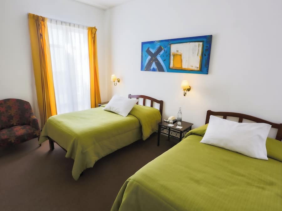 Una habitación de hotel con dos camas, una silla, un cuadro y una mesita de noche.