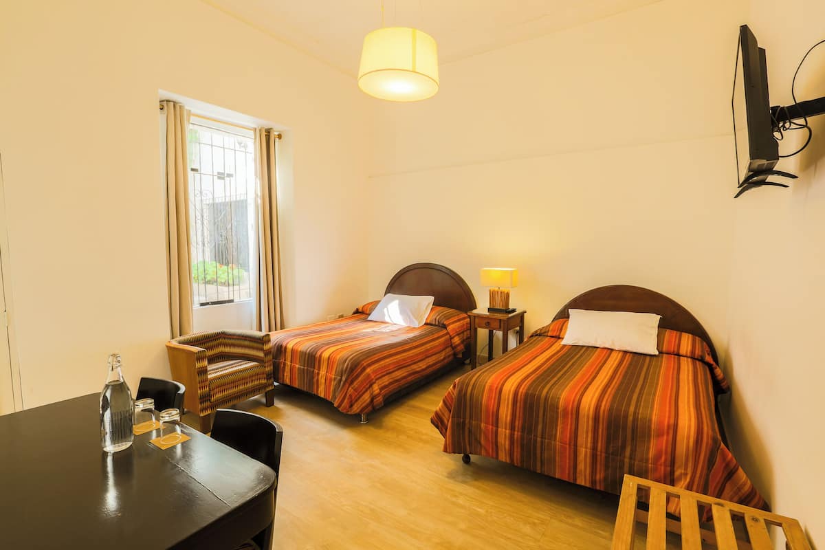 A hotel room with two beds, a desk, a chair, a lamp, and a TV mounted on the wall.