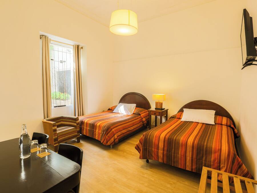 A hotel room with two beds, a desk, a chair, a lamp, and a TV mounted on the wall.