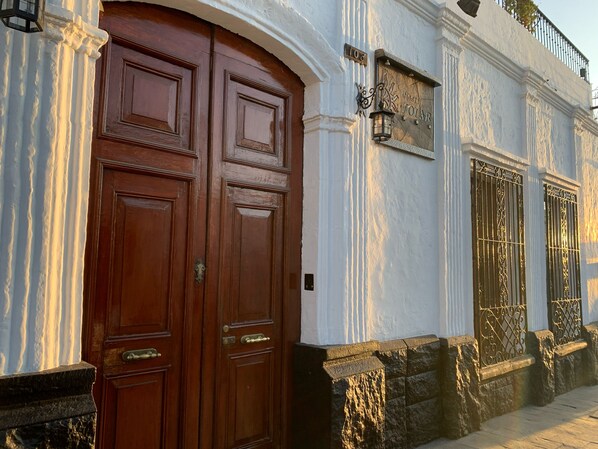A large wooden double door with a brass handle, flanked by white columns and a stone base. - Hostal Solar (Arequipa)