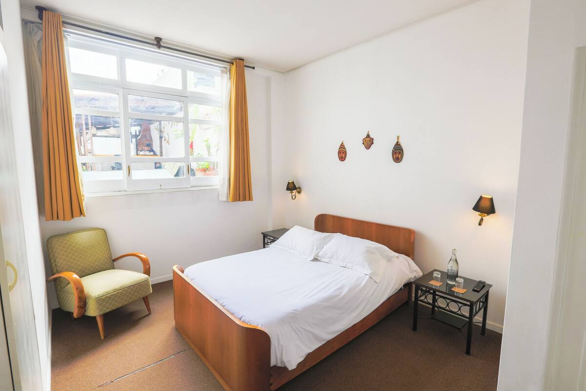 A bedroom with a bed, a chair, a nightstand, and a window with curtains.