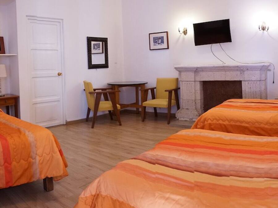 A hotel room with two beds, a fireplace, a TV, and a small table with chairs.