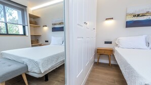 A modern bedroom with two beds, a bench, and a wooden floor.