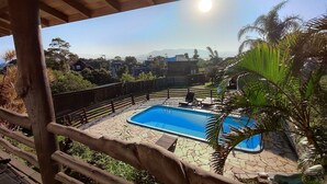 Un'area piscina con un solarium in legno, circondata da una recinzione e palme.