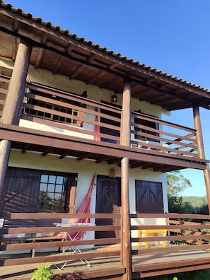 A two-story building with a balcony, wooden railings, and a door with a decorative design. - Pousada Casa Morango - Praia do Rosa (Imbituba)