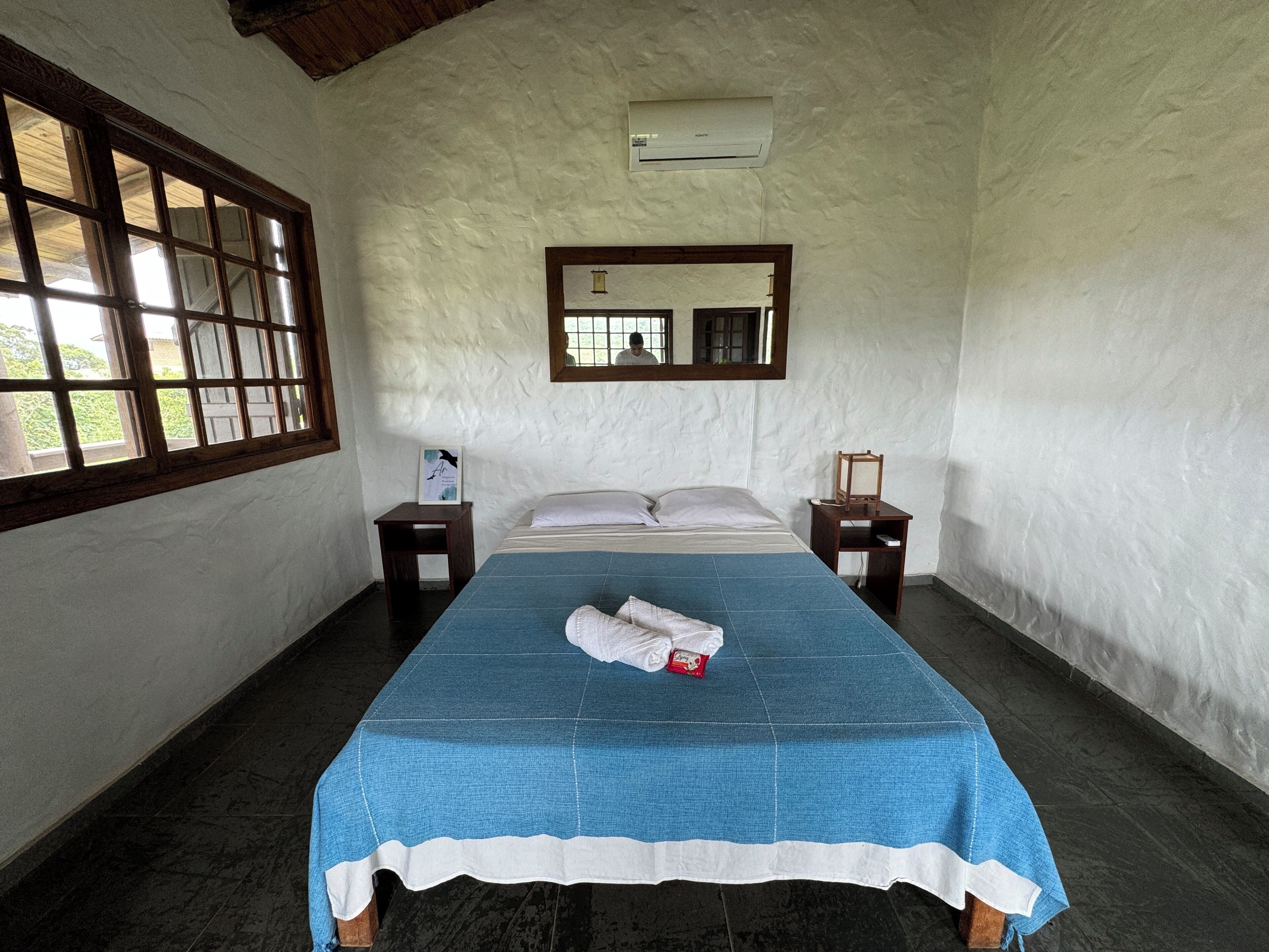 Ein Schlafzimmer mit einem Bett, einem Fenster, einem Spiegel und einer Wand-Klimaanlage.