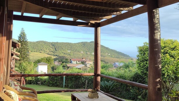 Une terrasse en bois, agrémentée de chaises et d’une table en osier, qui offre une vue panoramique sur un paysage pittoresque, avec des collines et des maisons.