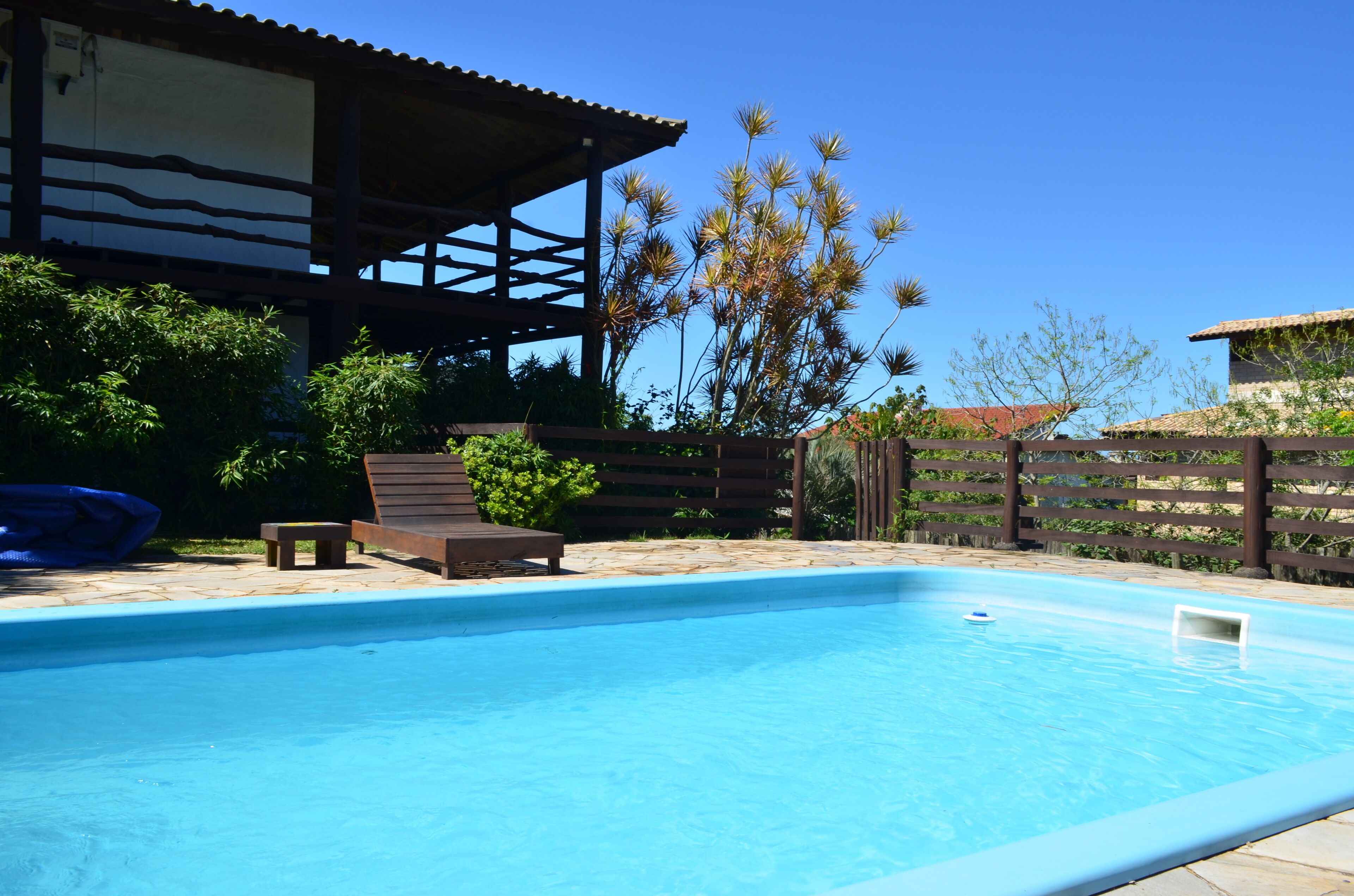 Una piscina con cubierta de madera, zona de estar techada y jardín cercado.