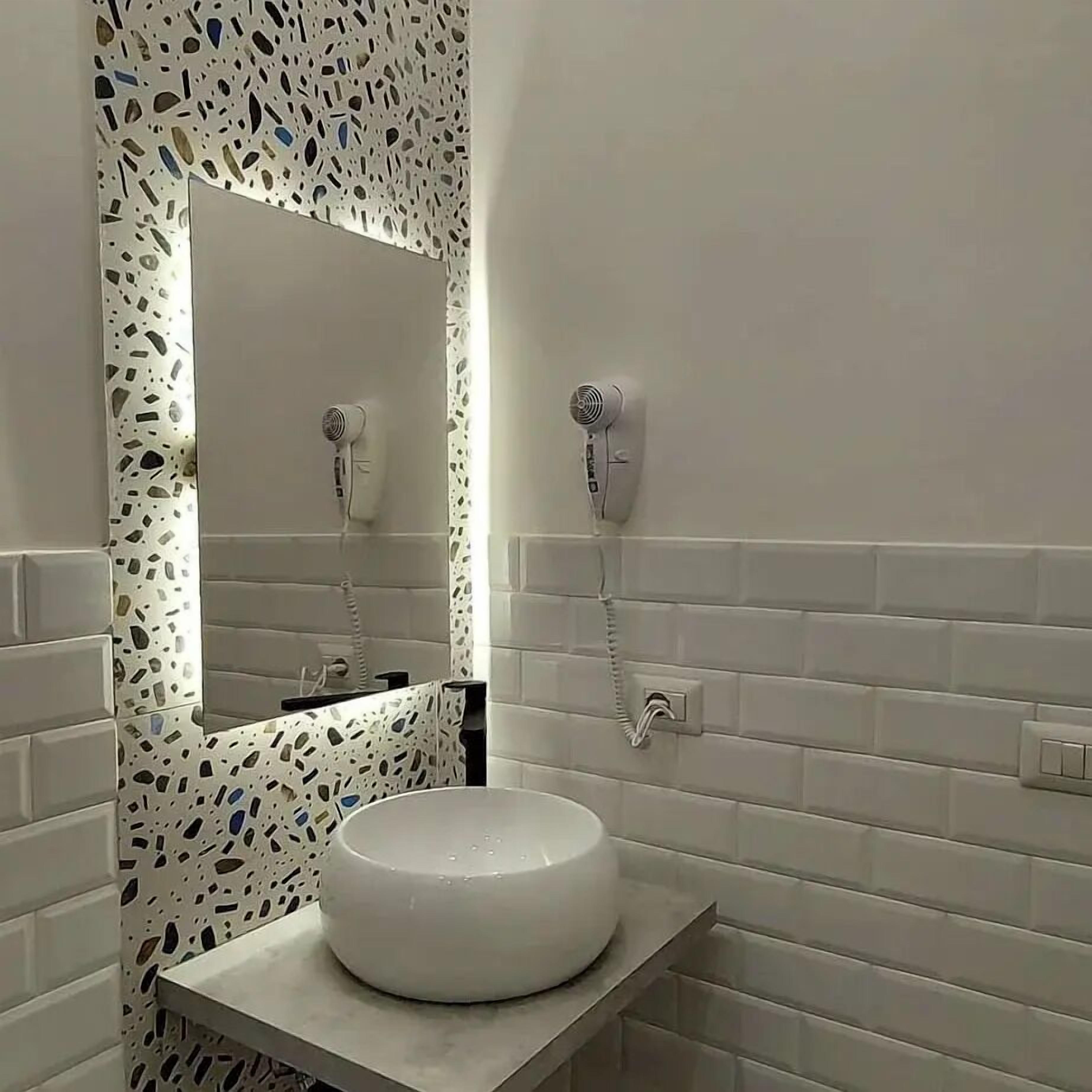 Une salle de bain avec un lavabo rond blanc, un miroir et deux sèche-cheveux fixés au mur.