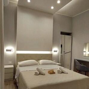 Una habitación de hotel moderna con una cama grande, mesitas de noche, un armario y un escritorio con una silla.