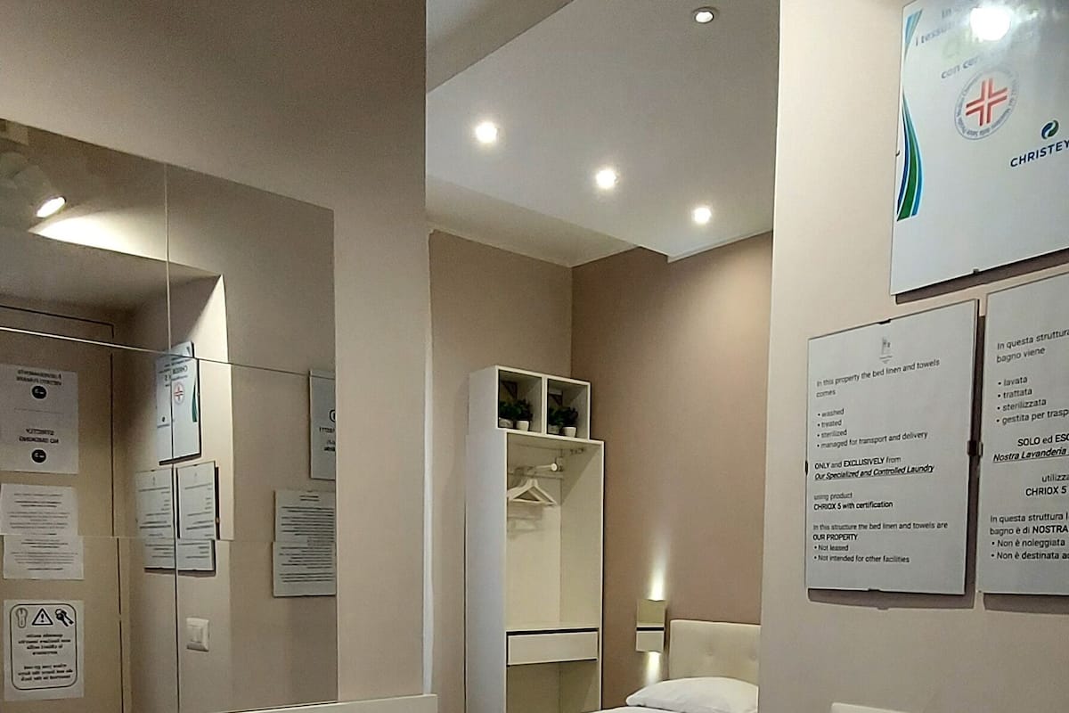 Habitación de hotel con cama, armario, espejo y pared decorada con carteles informativos.