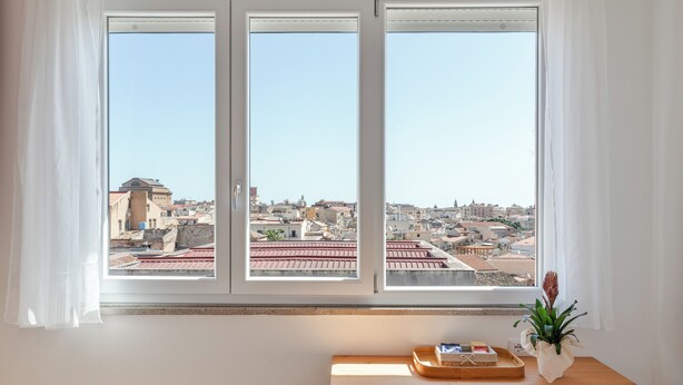 Une pièce dotée d’une grande fenêtre donnant sur la ville, d’un bureau en bois avec un plateau et d’une plante en pot.