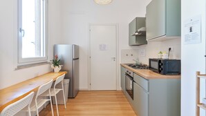 Une cuisine compacte avec un plan de travail en bois, un réfrigérateur, un four à micro-ondes et une cuisinière. Il y a une fenêtre qui laisse entrer la lumière naturelle et une porte sur laquelle est accrochée une note.