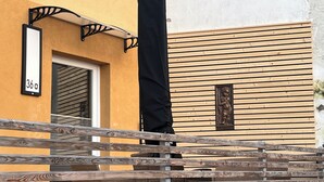 A wooden deck with a metal railing, a building with a yellow facade, and a black awning.
