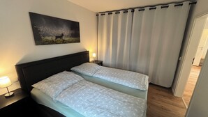A double bed with a headboard, a bedside table with a lamp, a painting on the wall, and a curtain.