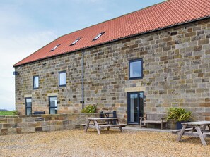 A stone building with a red-tiled roof, multiple windows, and outdoor seating. - Oak Cottage - UK48269 (Whitby)