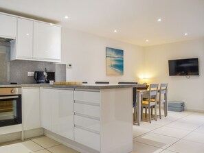 A modern kitchen with white cabinets, a central island, and a dining area with chairs and a table. - Oak Cottage - UK48269 (Whitby)