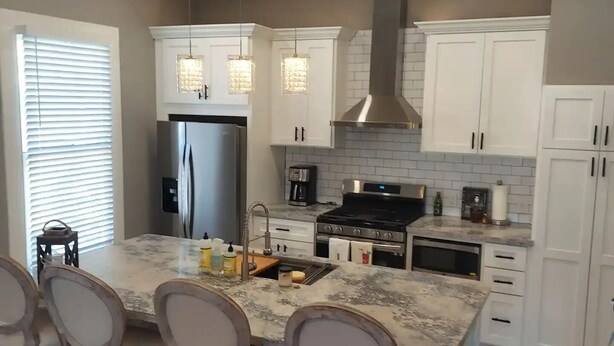 A modern kitchen with white cabinets, a stainless steel refrigerator, a gas stove, and a large island with bar stools.
