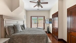A bedroom with a bed, a ceiling fan, a TV, and a door.