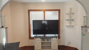A living room with a large flat-screen TV on a wooden stand, a gray sofa, and a patterned rug.