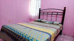 Une chambre avec des murs roses, un lit recouvert d’une couvre-lit à motifs, une fenêtre avec des rideaux blancs et un appareil de climatisation fixé au mur.