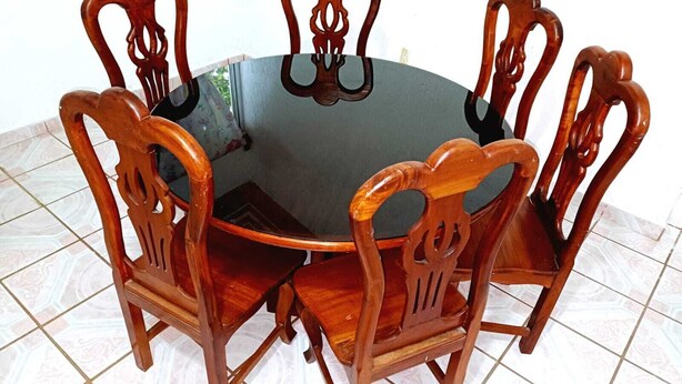 Une table de salle à manger ronde en bois, accompagnée de six chaises, chacune dotée d’un dossier en bois sculpté.