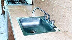 Une cuisine dotée d’un évier en acier inoxydable, d’une cuisinière à gaz et de murs carrelés.