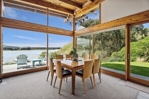 Enjoy meals in this spacious dining area with a large table and six chairs, offering a scenic view of the lake and lush greenery.