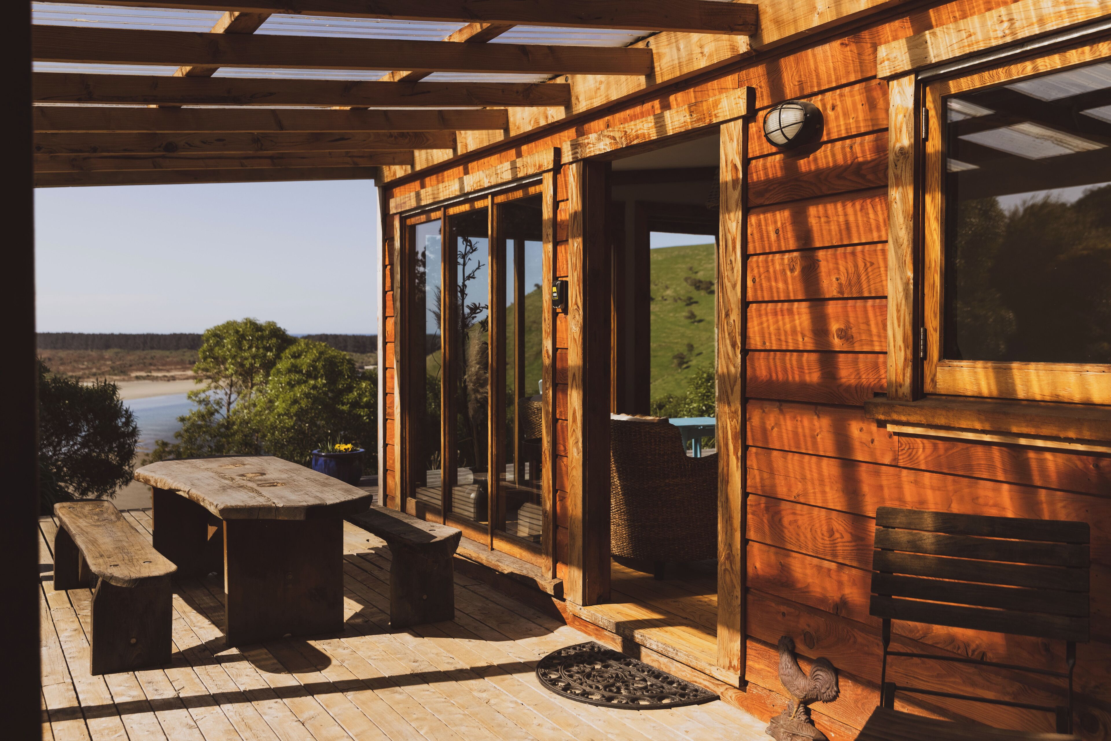 Une terrasse en bois avec une table et des bancs, donnant sur une étendue d’eau et une colline verdoyante.