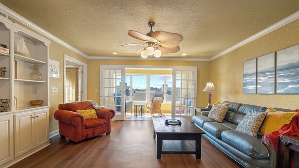 A spacious living room with a wooden floor, a ceiling fan, a sofa, a coffee table, and a bookshelf. - Condo at Sunbay Resort! Heated Pool & Hot Tub! (Hot Springs)